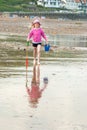 A young girl wears a pink floppy hat and carries a bucket and spade across a British beach Royalty Free Stock Photo