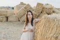 Young girl wears summer white dress near hay bale in field. Beautiful girl on farm land. Wheat yellow golden harvest in autumn Royalty Free Stock Photo