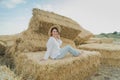Young girl wears summer white dress near hay bale in field. Beautiful girl on farm land. Wheat yellow golden harvest in autumn Royalty Free Stock Photo