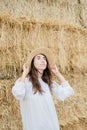 Young girl wears summer white dress near hay bale in field. Beautiful girl on farm land. Wheat yellow golden harvest in autumn Royalty Free Stock Photo