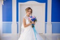 A young girl in a wedding dress stands against the blue-blue walls and presses a bouquet of flowers to her. A beautiful Royalty Free Stock Photo