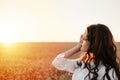 Young girl in wheat field at sunset. Curly-haired brunette white Caucasian girl watching the sunset in the field. Slow living life