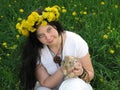 A young girl in white clothes with long black hair and a wreath of dandelions sits on a bright green field with dandelion flowers Royalty Free Stock Photo