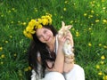 A young girl in white clothes with long black hair and a wreath of dandelions sits on a bright green field with dandelion flowers Royalty Free Stock Photo