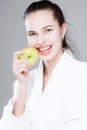 A young girl in a white coat bites a green apple while holding it in her hand. Healthy teeth concept Royalty Free Stock Photo