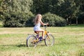 Young girl in white dress riding her bicycle in summer park on meadow with green grass Royalty Free Stock Photo