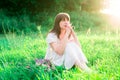 Young girl in white dress sitting in the middle of the field and reflects. Sadness, loneliness, doubt.