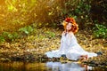 Young girl in white dress sitting on the river Bank in a wreath of yellow leaves in Sunny autumn day Royalty Free Stock Photo