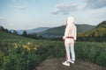 A young girl in a white tracksuit looks into the distance at the beautiful mountains in the early evening. Climbing the mountain.