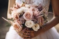 young girl in a white wedding dress holds in her hands a bouquet of flowers and greenery with a ribbon Royalty Free Stock Photo