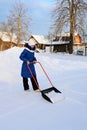 young girl in winter clothes cleans snow with shovel in countryside. Teenage girl with large scraper helps adults to remove snow Royalty Free Stock Photo