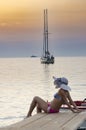 Young girl woman in bikini with hat sitting at wooden pier and looking on the sea sunset Royalty Free Stock Photo