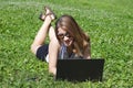 A young girl or woman lies on a meadow in the park and works on a laptop. Freelance, education or working online concept Royalty Free Stock Photo