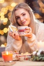 A young girl in a wool sweater holding a gingerbread and a cup with tea coffee or Christmas punch Royalty Free Stock Photo