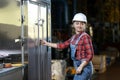 Young girl in a work dress and white hard hat in a factory. Woman in a work uniform holding reflective vest in a storage. Working