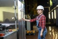 Young girl in a work dress and white hard hat in a factory. Woman in a work uniform. Working process.