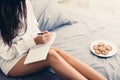 Young woman sitting on her cozy bed and making notes Royalty Free Stock Photo