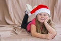 Little smiling girl in a red t-shirt with a santa claus hat lies on her stomach and smiles Royalty Free Stock Photo