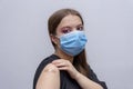 A young girl 18-20 years old in a medical mask points to a bandage with a vaccine against COVID-19, a coronavirus vaccination prog Royalty Free Stock Photo