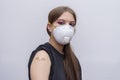 A young girl 18-20 years old in a medical mask points to a bandage with a vaccine against COVID-19, a coronavirus vaccination prog Royalty Free Stock Photo