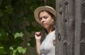 A young girl of 17-20 years old in a white dress and a straw hat smiles and opens a wooden door, leaving a rural house. Royalty Free Stock Photo