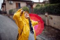 A young girl in a yellow raincoat and with pink umbrella who is walking the street is in a good mood while enjoying music and rain Royalty Free Stock Photo