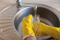 A young girl in yellow rubber gloves washes a glass glass under running tap water in the kitchen Royalty Free Stock Photo