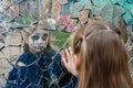 Young girl zombie looks in a broken mirror and shows her hand on a mirror. Halloween and day of the dead concept Royalty Free Stock Photo