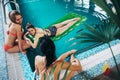 Young girlfriends wearing swimwear relaxing in swimming-pool talking and smiling