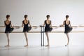 Young girls, ballet dancers in black attire and pointe standing next to barre and training, practicing against grey