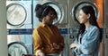 Mixed-races stylish young girls best friends talking and sharing secrets while standing in public laundromat. Royalty Free Stock Photo