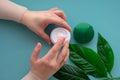 Young girls hand nearby white soft cream in jar with green leaves.