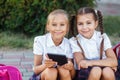 Young girls reading an ebook. Pupils of primary school. Girls with backpacks near building outdoors. Beginning of lessons. First d