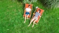 Young girls relax in summer garden in sunbed deckchairs on grass, women friends have fun outdoors in green park on weekend