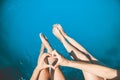 Young girls sit on the edge of swimming pool and chat with their feet in the water and hold their hands in heart Royalty Free Stock Photo