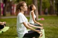 Young girls sit in the lotus positions doing yoga on yoga mats on green grass in the park on a warm day