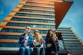 Young girls in sunglasses sitting on a city street and drink coffee to take away. Three cute women have a coffee break together