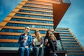 Young girls in sunglasses sitting on a city street and drink coffee to take away. Three cute women have a coffee break together