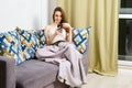 Young glad pleased woman relaxing on cozy sofa with smartphone at home in evening Royalty Free Stock Photo