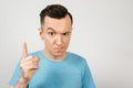 Young gloomy threaten man with a finger, dressed in a blue t-shirt on a light background. Close up portrait Royalty Free Stock Photo