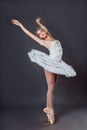 A young graceful ballerina dressed in professional attire, pointe shoes and a white tutu, demonstrates dance skills. Beautiful