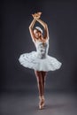 A young graceful ballerina dressed in professional attire, pointe shoes and a white tutu, demonstrates dance skills. Beautiful