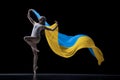 Young graceful classic ballerina dancing with cloth painted in blue and yellow colors of Ukraine flag on dark studio