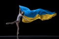 Young graceful classic ballerina dancing with cloth painted in blue and yellow colors of Ukraine flag on dark studio