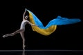 Young graceful classic ballerina dancing with cloth painted in blue and yellow colors of Ukraine flag on dark studio