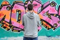 A young graffiti artist in a gray hoodie looks at the wall with