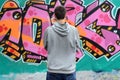 A young graffiti artist in a gray hoodie looks at the wall with