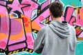 A young graffiti artist in a gray hoodie looks at the wall with