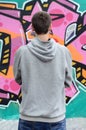 A young graffiti artist in a gray hoodie looks at the wall with