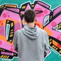 A young graffiti artist in a gray hoodie looks at the wall with